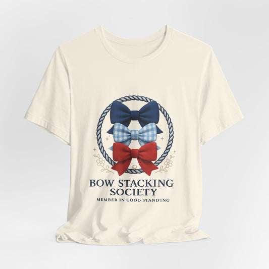 Cream T-shirt featuring Bow Stacking Society logo with stacked bows in red and blue and rope motif.